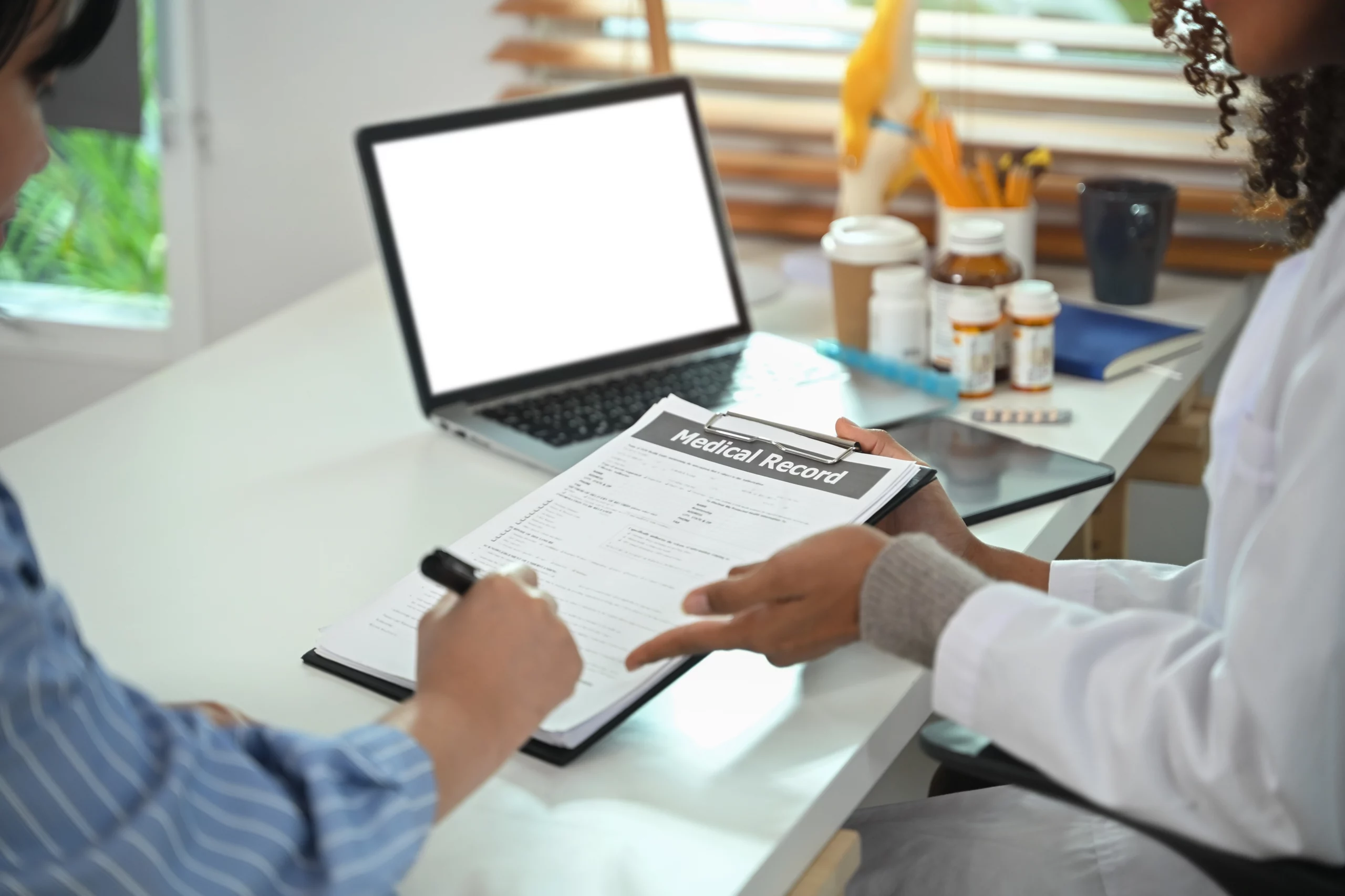 A doctor in a white coat points to a medical record on a clipboard as a patient signs it, symbolizing the health care proxy process.